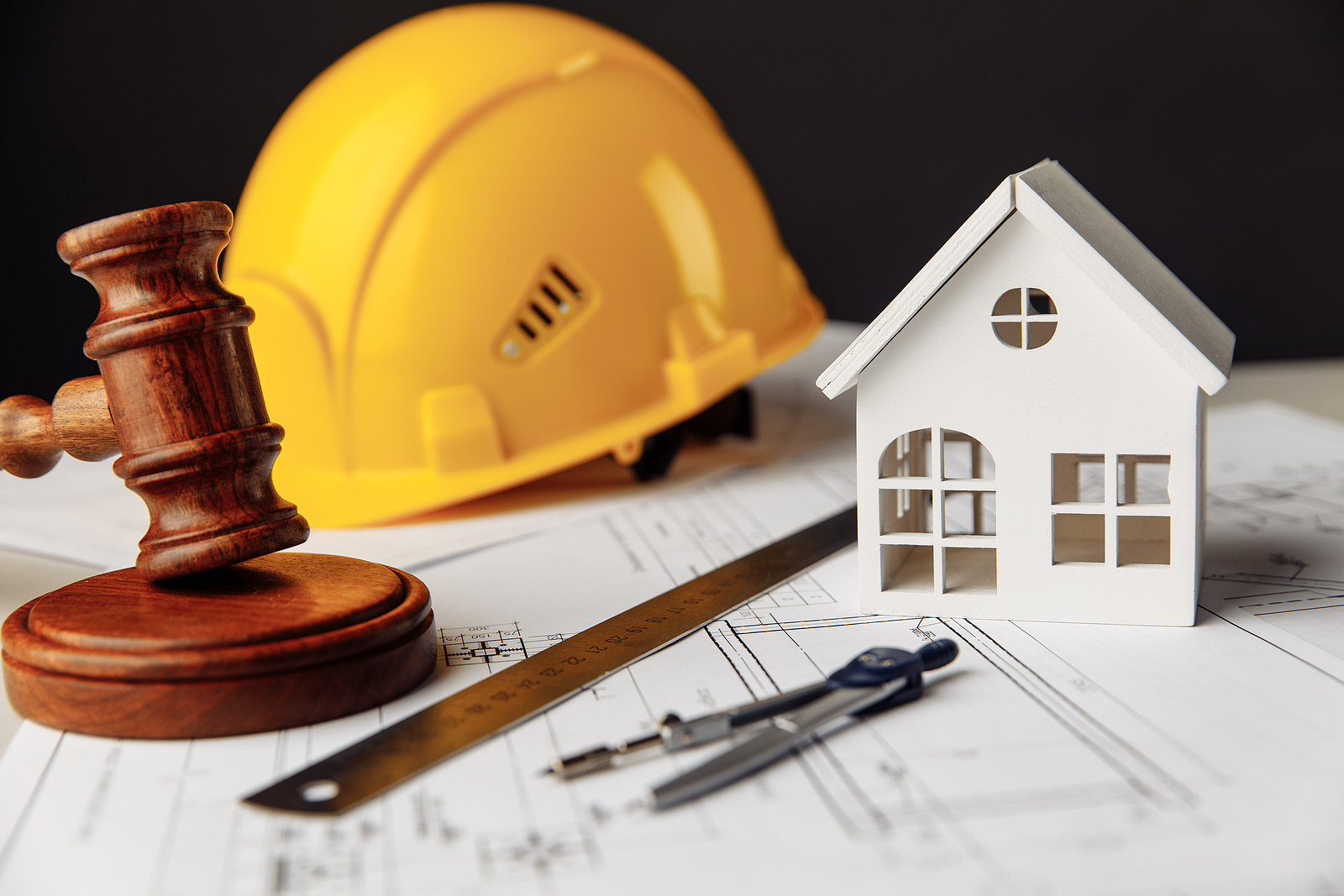 Judge gavel, white house and yellow hard hat with drawing tools on construction plan. Law concept